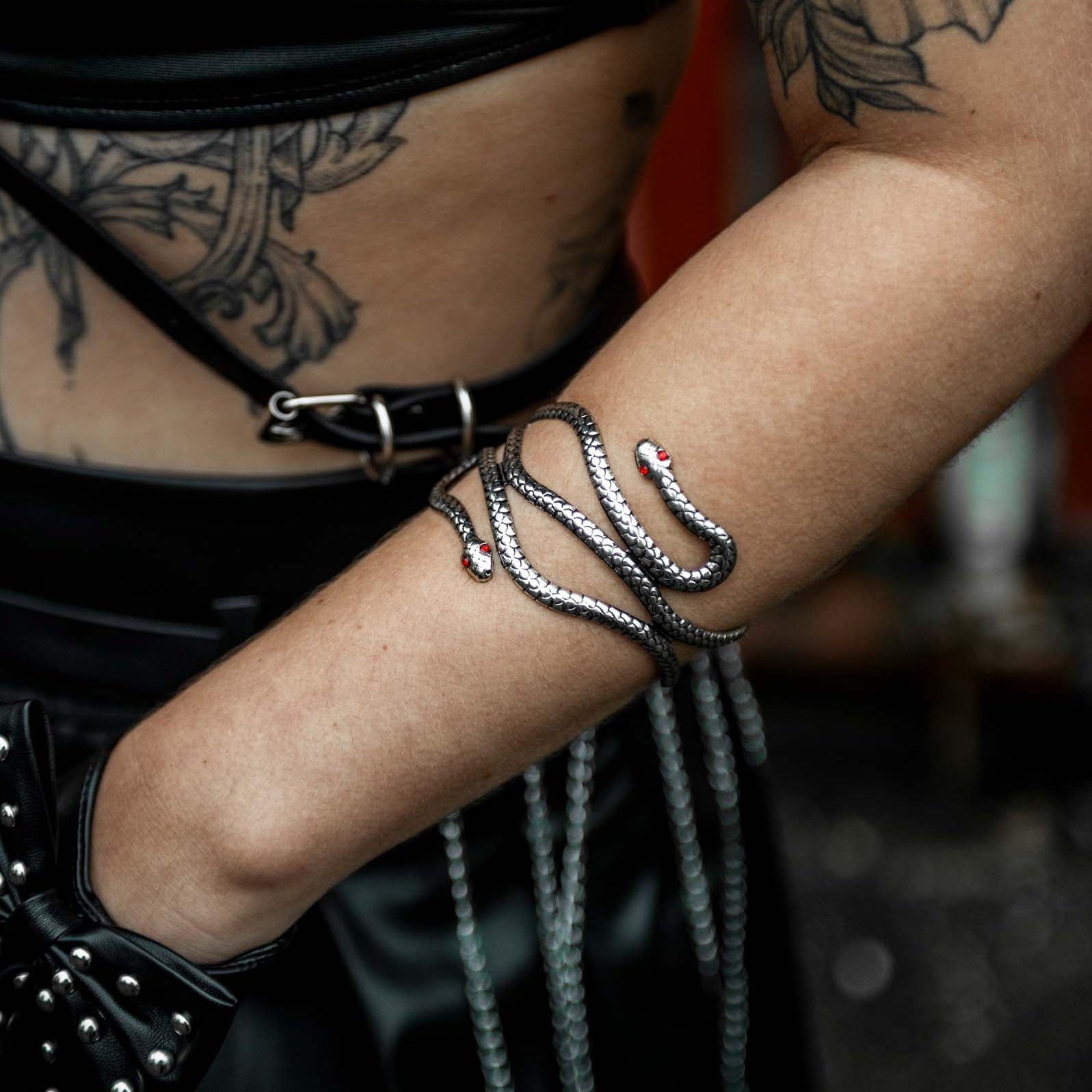 vrouwelijk model met close up arm met rave armband 'iron snake'. Een slang met rode steentjes als ogen
